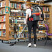 A woman using a NaceCare cordless backpack vacuum to clean a book shelf.