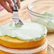 A person's hand with a knife cutting a cake with white frosting.