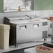 A stainless steel two-door refrigerated pizza prep table with a white cutting surface and closed top compartments.