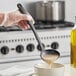 A hand holding a black Choice ladle over a bowl of liquid.