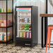 A black refrigerated glass door merchandiser with LED lighting, stocked with various beverages.