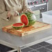 A person cutting a watermelon in half on a Choice wood cutting board.