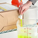 A hand pouring yellow Betco floor cleaner from a red container into another container.