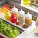 A stainless steel tray holding condiment bottles and vegetables.