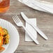 A white plastic fork and knife on a napkin on a plate of food.