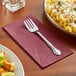 A fork on a burgundy Hoffmaster paper dinner napkin next to a plate of pasta and salad.