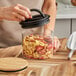 A person using a spoon to put fruit in a Planetary Design Airscape food storage container on a kitchen counter.