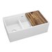 A Zurn white fireclay double bowl farmhouse sink with a wooden cutting board over one bowl.