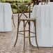 A Lancaster Table & Seating Vineyard Series whiskey brown wood cross back bar stool on a table with a white tablecloth outside.