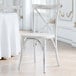 A Lancaster Table & Seating rustic white cross back chair sitting in front of a table.