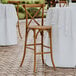 A Lancaster Table & Seating Vineyard Series Barrel Brown Wood Outdoor Cross Back Bar Stool on a brick patio with a white table.