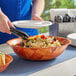 A woman using tongs to put food in a Choice woven wood salad bowl.