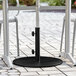 A black Lancaster Table & Seating round steel umbrella base on a brick patio.