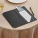 An American Metalcraft black leather check presenter with gold corners holding a bill, pen, and credit cards.