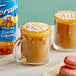 A glass mug of coffee with caramel syrup next to a Torani Sugar-Free Classic Caramel Flavoring Syrup bottle.