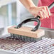 A person using a Choice flat wire carbon steel bristle grill brush head to clean a metal grate.