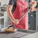 A person in a red apron using a Choice grill brush to clean a charbroiler.