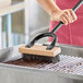 A person using a Choice stainless steel bristle grill brush to clean a grill.