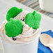 A white cup of ice cream with Vidal green apple gummies on top.