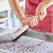 A person using a Choice stainless steel wire bristle grill brush to clean a grill.