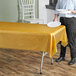 A woman holding a white plate over a Table Mate gold plastic table cover on a table.