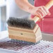 A person using a Choice carbon steel brush head to clean a grill.