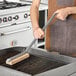 A person using a Choice steel bristle grill brush to clean a grill.