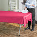 A woman holding a white plate over a hot pink Table Mate plastic table cover on a table.