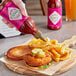 A hand pouring TABASCO Sweet & Spicy Hot Sauce onto a burger and fries.
