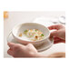 A hand holding a Libbey white porcelain grapefruit bowl filled with food.