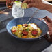 A hand holding a lime wedge over a bowl of food on a table with a Libbey blue terracotta bowl.