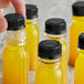 A person's finger holding a black plastic bottle of yellow liquid.