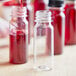 A person pouring red liquid from a glass into small clear PET bottles.