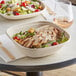 A table set with two World Centric compostable bowls filled with salads, one with grilled chicken and tomatoes.