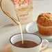 A cup of coffee and a muffin on a table with a container of Planet Oat Original Oat Milk.