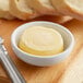 A bowl of Echire butter next to a knife on a wooden surface.