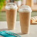 Two Choice clear plastic cups of coffee with straws on a table.