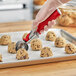 A hand using a Fourté red thumb press disher to scoop cookie dough.