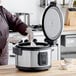 A woman using an Avantco commercial electric rice cooker to cook rice.