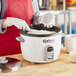 A woman in a red apron using an Avantco commercial rice cooker to prepare food.