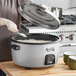 A woman using an Avantco stainless steel lid to cook rice in a large rice cooker.