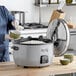 A woman using an Avantco electric rice cooker to pour rice into a bowl.