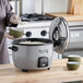 A woman using an Avantco stainless steel lid to cook rice in a rice cooker.