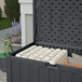 A black Suncast resin outdoor storage box with a lid open and white and grey pillows inside.