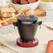 A person holding a stick over a small black pot with a marshmallow on it using the Valor tabletop cast iron grill.