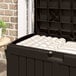 A black Suncast outdoor storage box with white striped cushions inside.