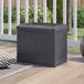 A grey plastic Suncast deck box with a lid on a patio.