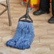 A person's leg and black shoes using a Lavex Pro Blue Rayon Blend Looped End Mop.