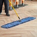 A person using a Lavex blue cotton blend dry dust mop with looped ends to clean a floor.