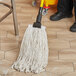 A person cleaning a floor with a Lavex White Rayon Cut-End Mop Head.